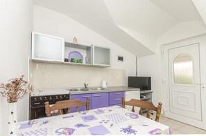 Une cuisine de taille réduite, équipée d’une cuisinière, d’un évier et de placards, une table à manger avec des chaises, et un téléviseur placé dans un coin.