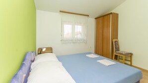 A bedroom with a bed, a chair, a wardrobe, and a window with curtains. - Apartments Mira I (Vodice)
