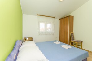 A bedroom with a bed, a chair, a wardrobe, and a window with curtains. - Apartments Mira I (Vodice)