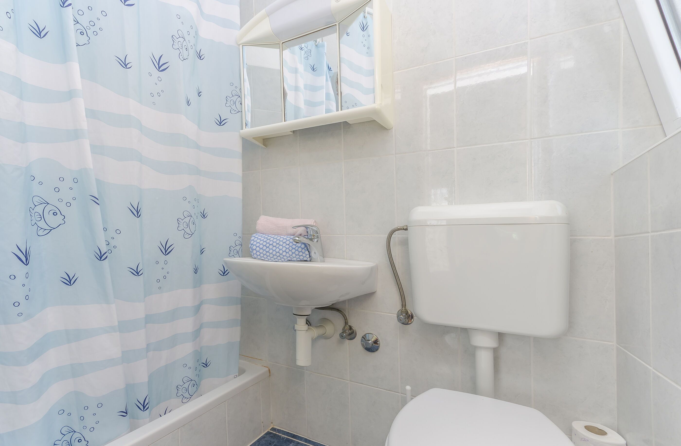 A bathroom with a shower curtain, a sink, a toilet, and a mirror.