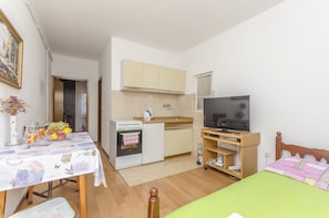 A compact room with a kitchenette, a dining table, a TV, and a bed.