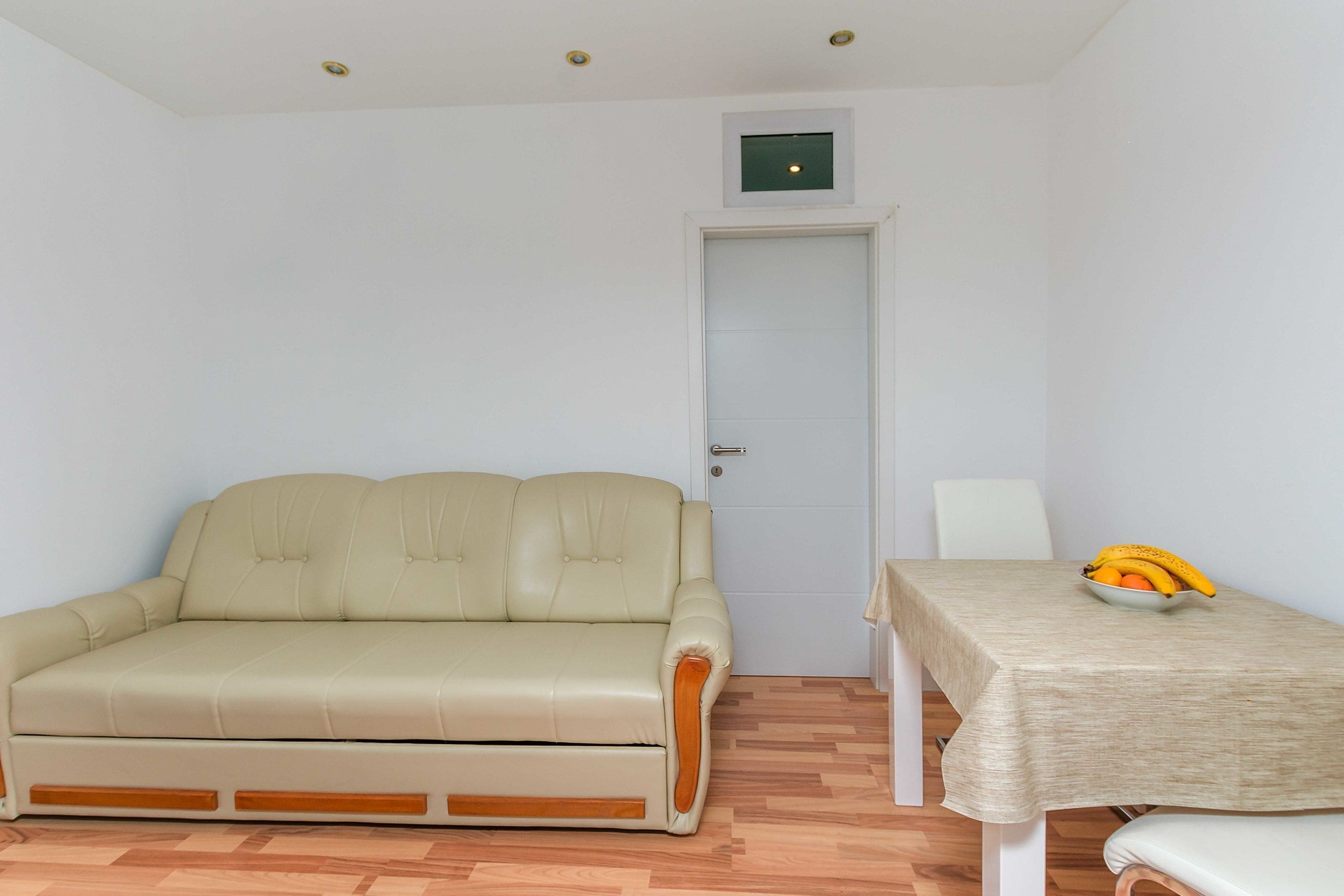 Ein Zimmer mit einem beigen Sofa, einem Tisch mit Obstschale und einer Tür.