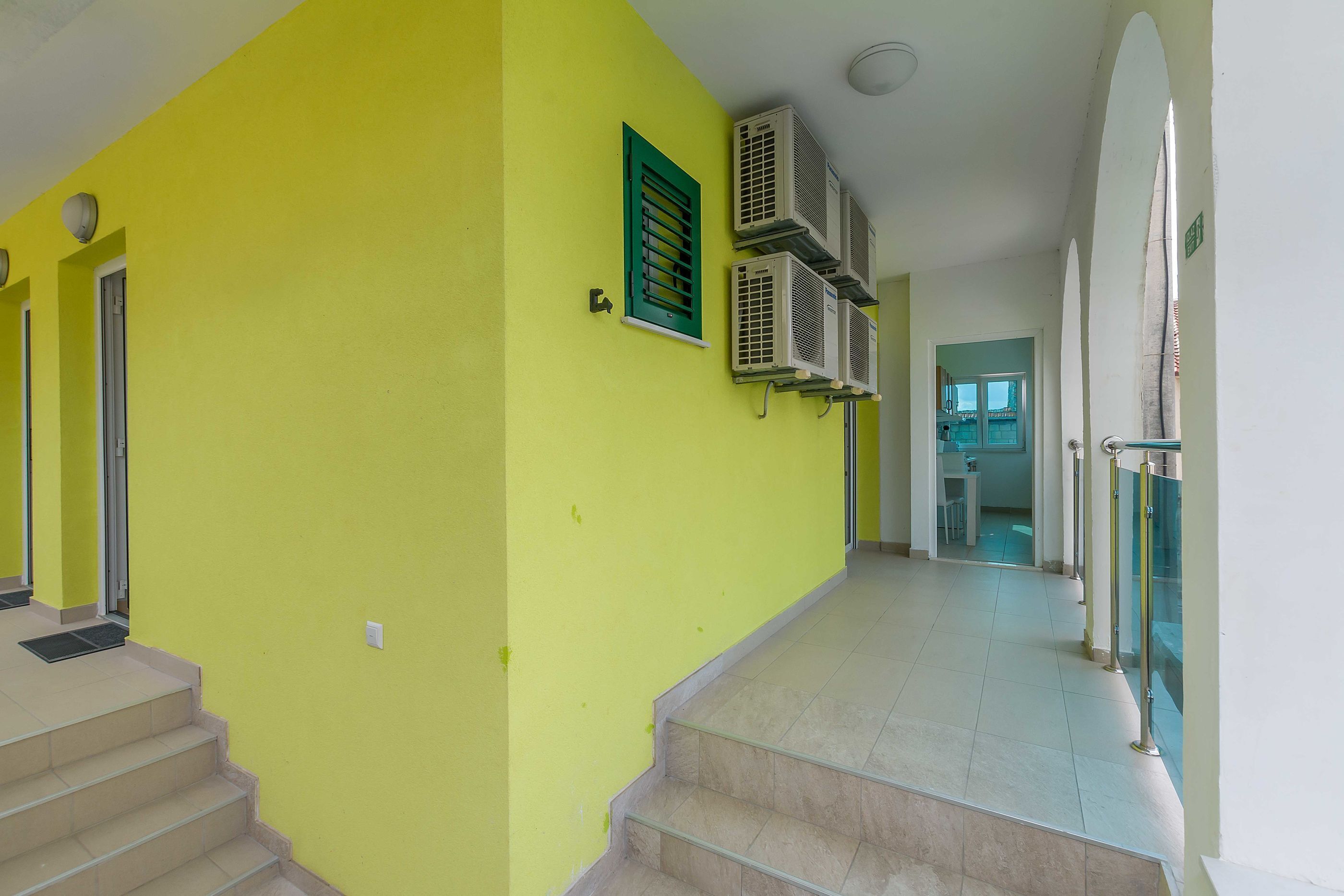 Um corredor amarelo vibrante com escada, unidades de ar condicionado e guarda-corrimão de vidro.