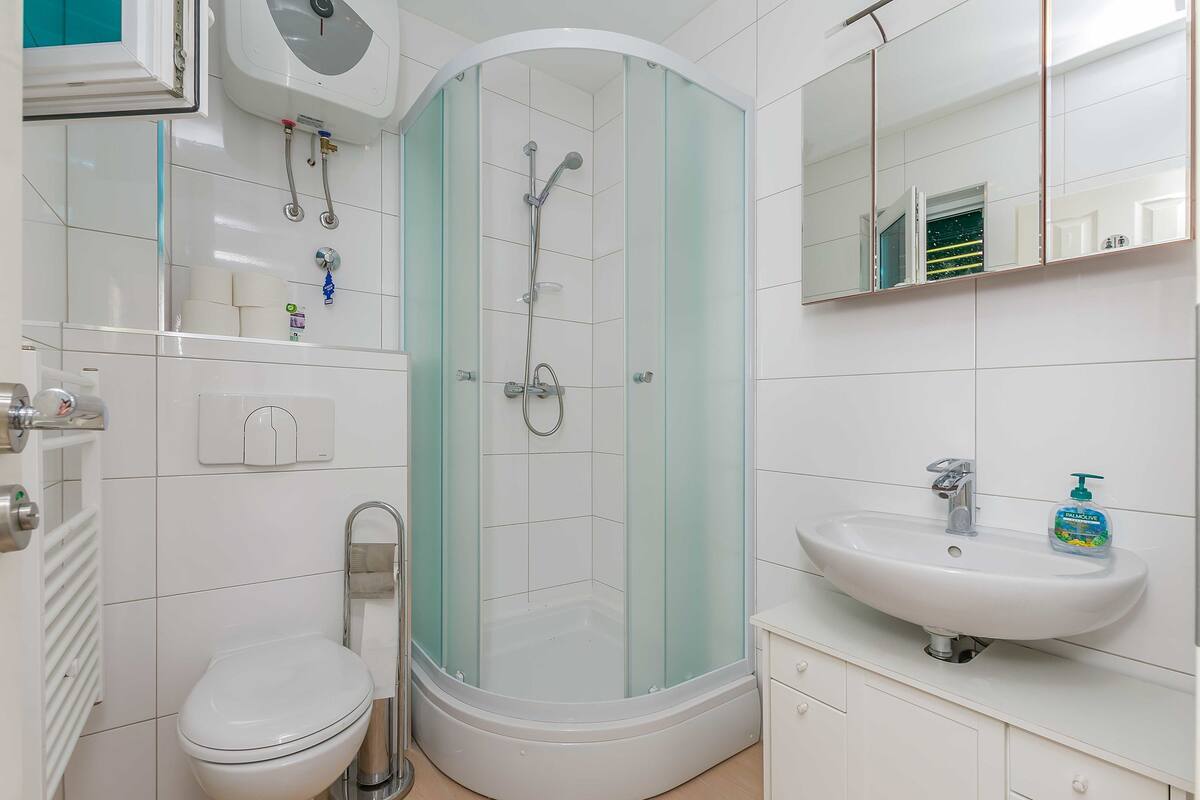 A modern bathroom with a glass-enclosed shower, a white toilet, a sink with a soap dispenser, and a mirror above the sink.