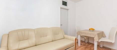 A room with a beige sofa, a dining table with a bowl of fruit, and a white door.
