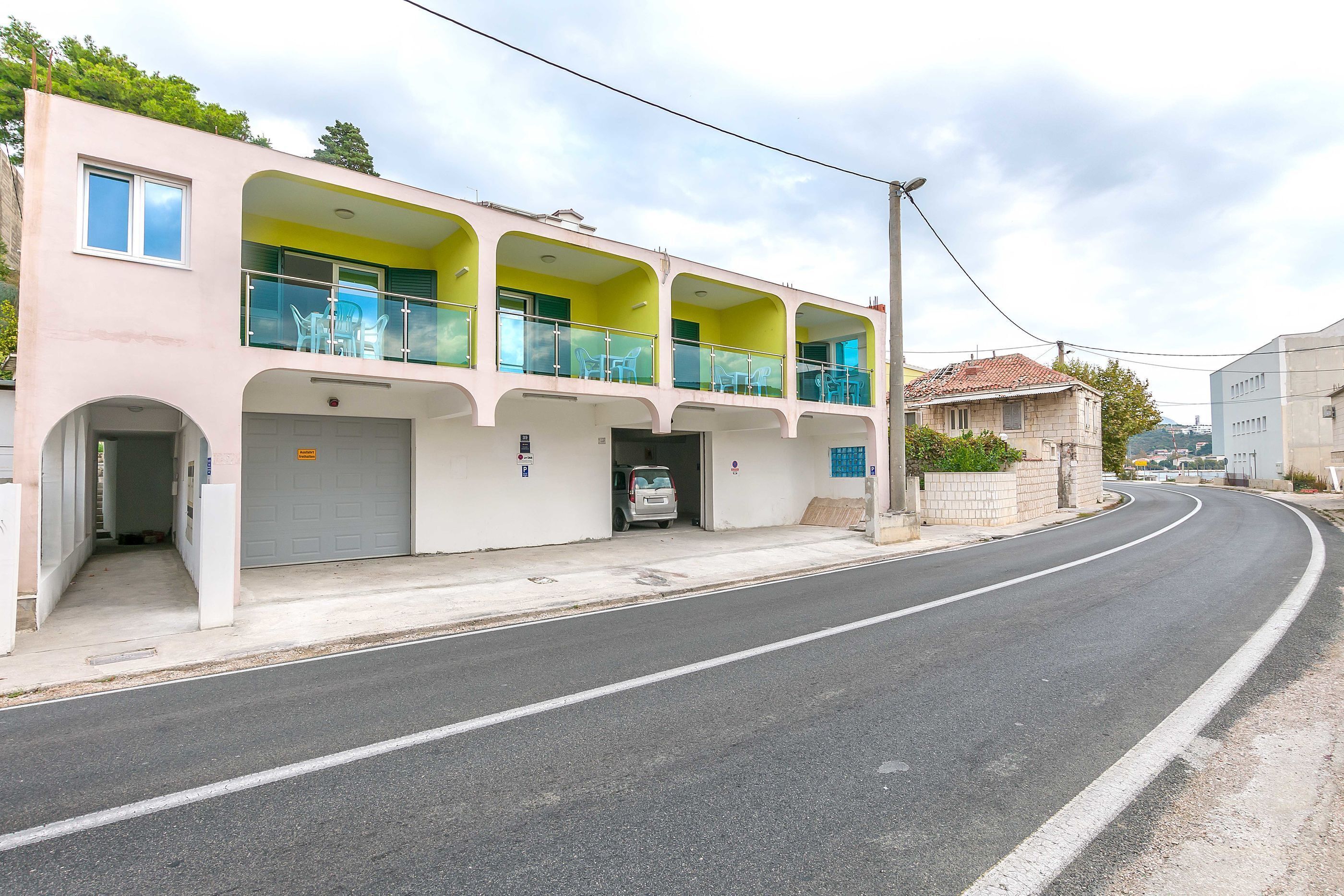 A two-story building with balconies, a garage, and a clear road in front.