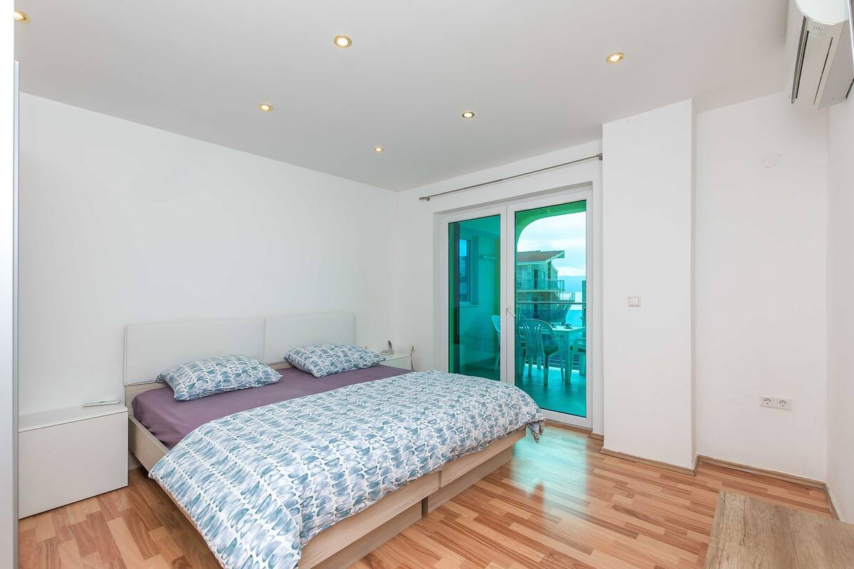 A bedroom with a bed, a nightstand, and a sliding glass door leading to a balcony.
