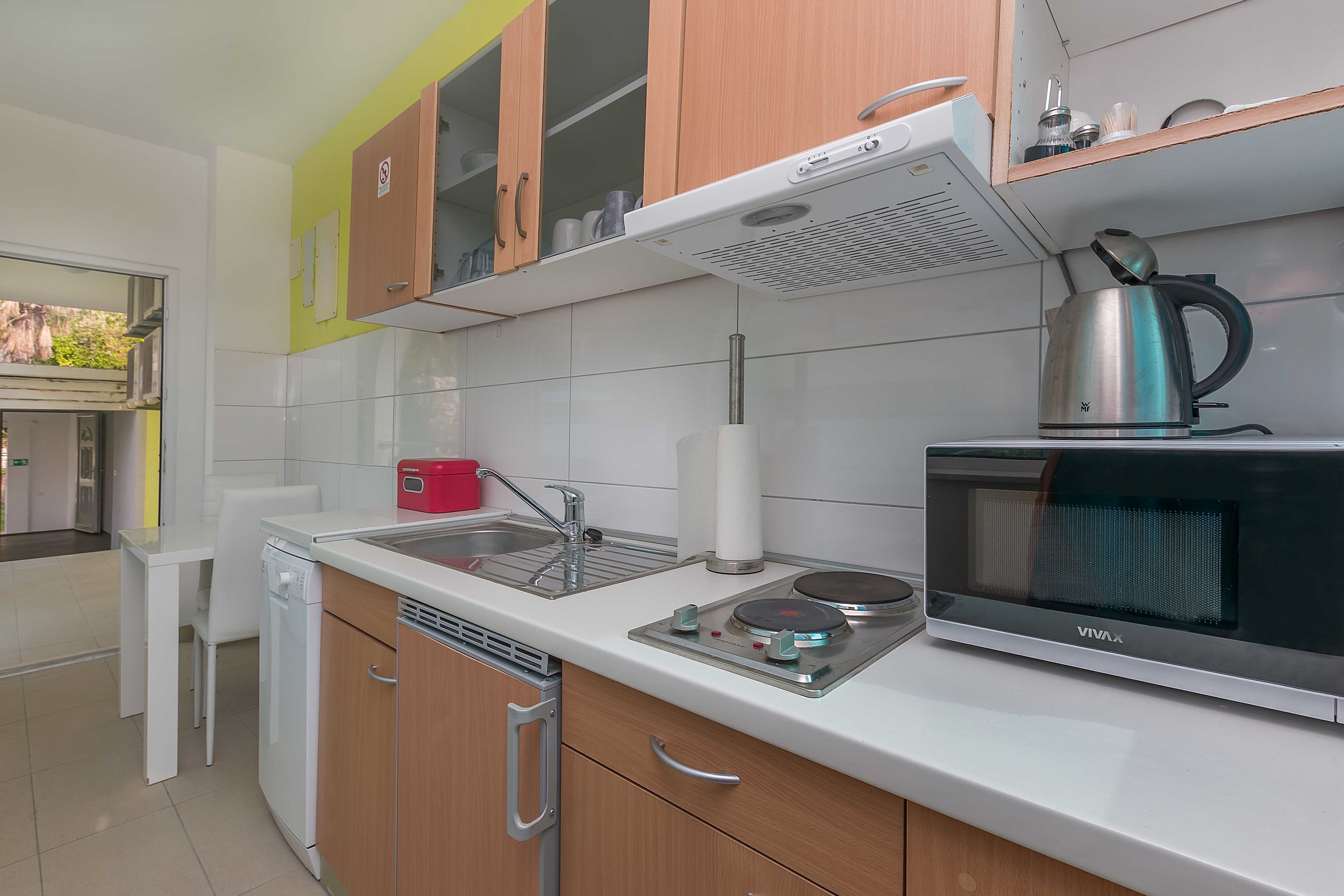 A modern kitchen with a dishwasher, a sink, a kettle, and a microwave.