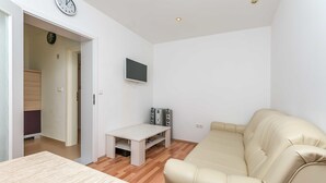 Uma sala de estar moderna com um sofá bege, uma mesinha branca e uma TV fixada na parede.