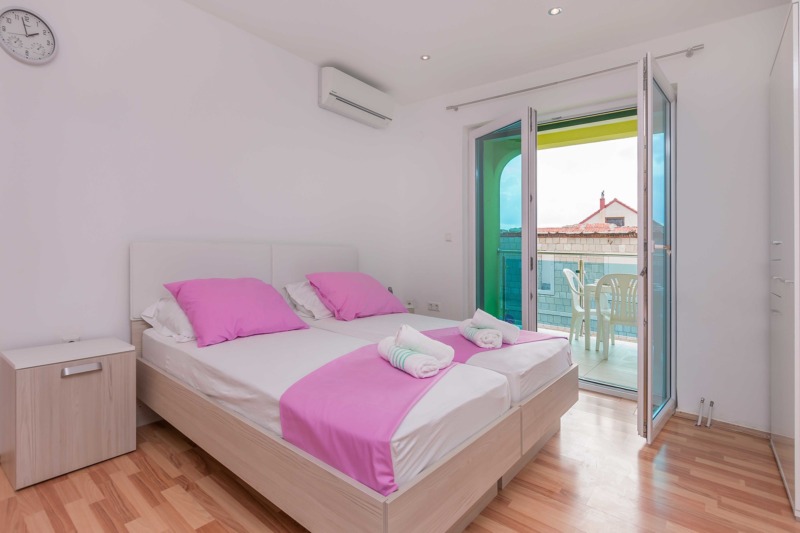 A double bed with pink bedding, a bedside table, and a window with a view of a balcony.