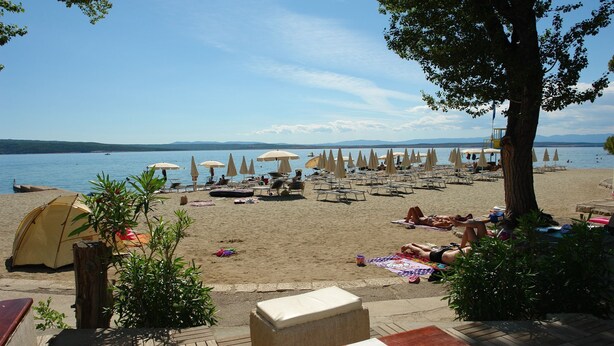 Une plage avec des tentes, des chaises longues et des parasols.