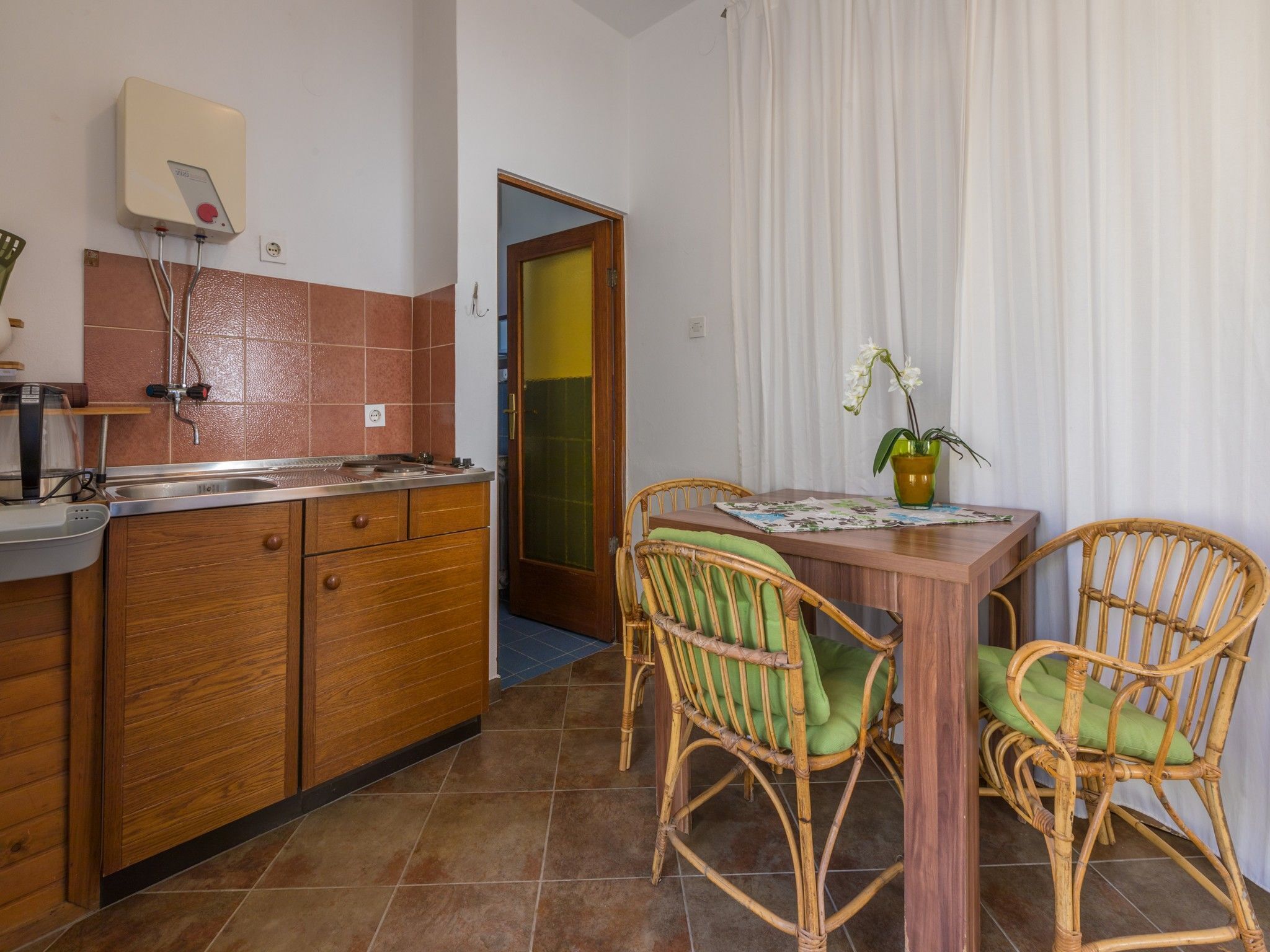 A compact kitchen with wooden cabinets, a built-in sink, and a small dining area with wicker chairs and a table.