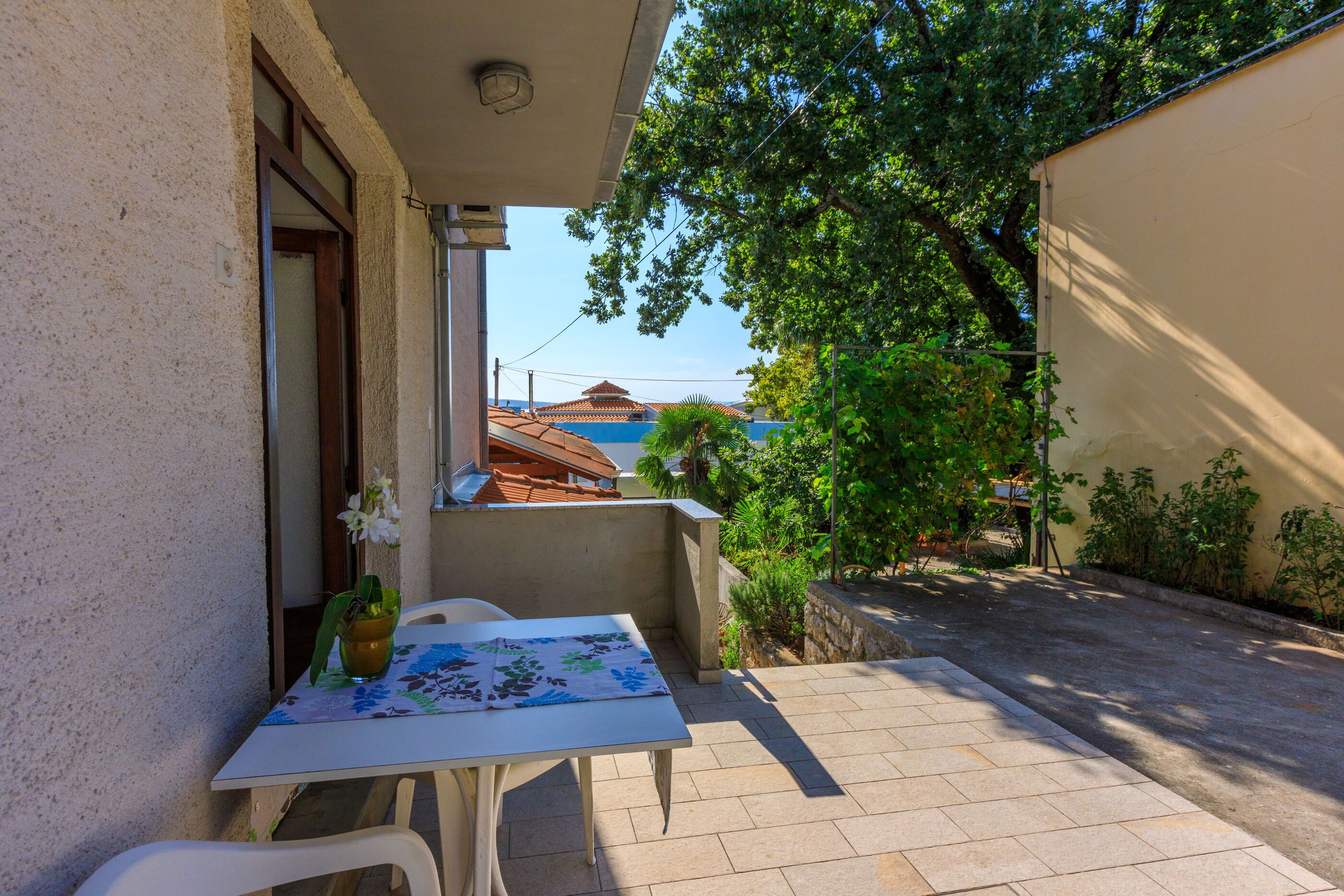 Une petite terrasse extérieure avec une table et des chaises, un pot de fleurs et une vue sur des bâtiments en arrière-plan.