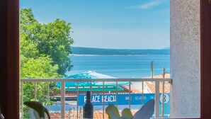 Un balcon avec vue sur la mer, une pancarte indiquant «
Plage de la Paix
», et des fleurs blanches au premier plan.
