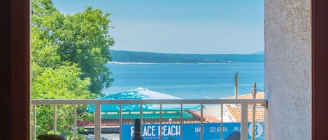 En balkong med utsikt över havet, en skylt med texten ”Peace Beach”, och vita blommor i förgrunden.