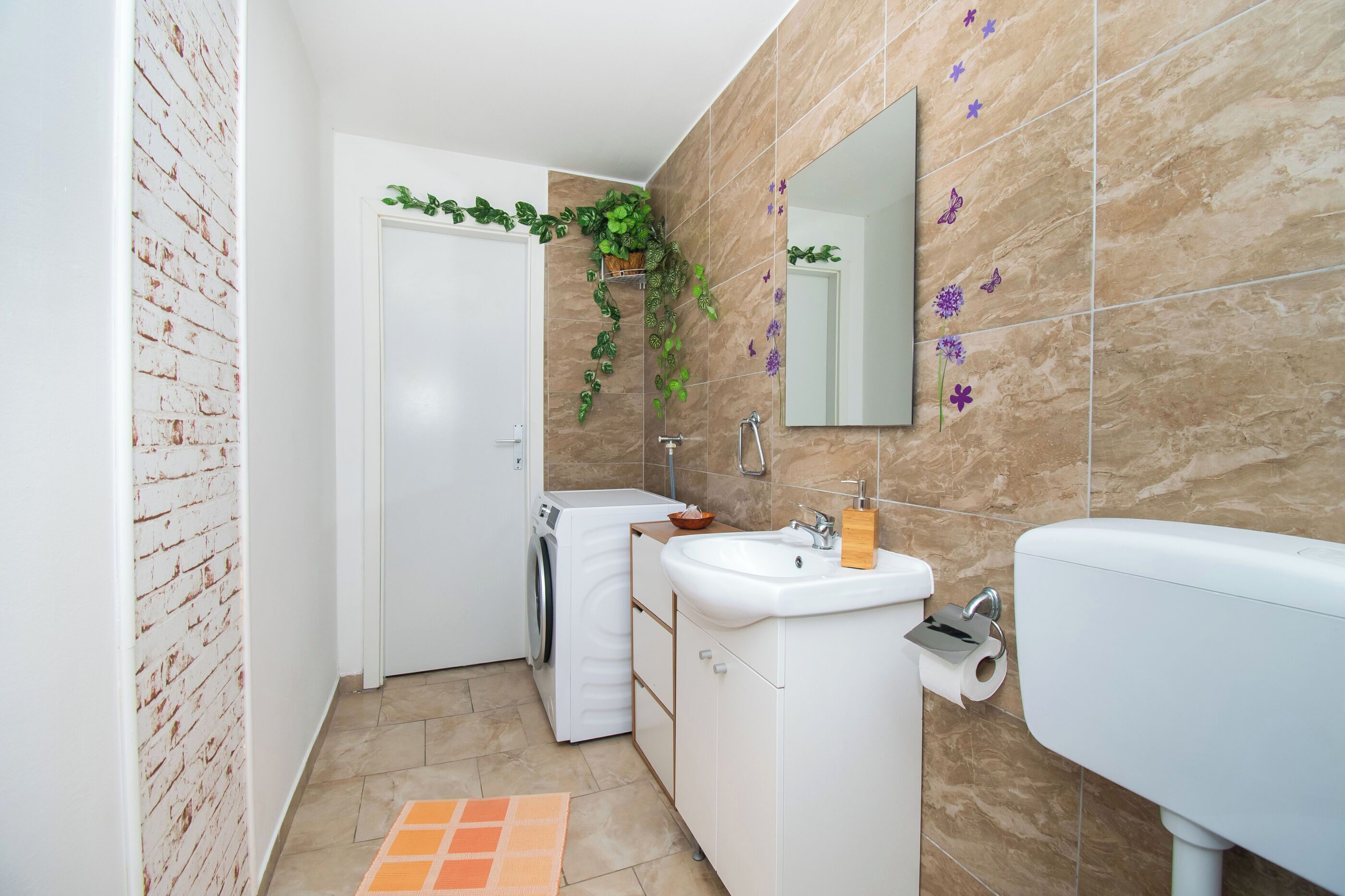 A compact bathroom with a washing machine, a sink, and a mirror.