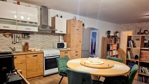 Eine kompakte Küche mit Herd, Mikrowelle und Kühlschrank. Ein Esstisch mit Stühlen und eine Bücherwand mit Büchern.