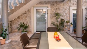 Eine Terrasse mit Steinsäulen, einem Tisch mit Glasplatte, Korbstühlen und Topfpflanzen.