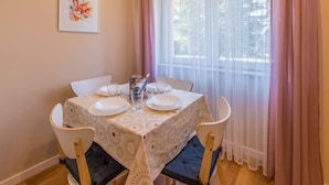 A dining table set with plates, glasses, and a bottle, surrounded by chairs, with a window and curtains in the background.