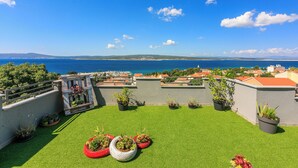 Eine Dachterrasse mit Kunstgrasanlage, Topfpflanzen und Blick auf das Meer und ferne Hügel.