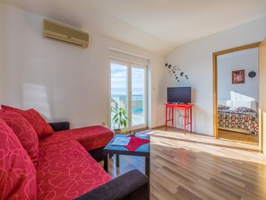 Een woonkamer met een rode bank, een kleine tafel, een televisie op een rode standaard en een balkon met uitzicht op een zwembad.