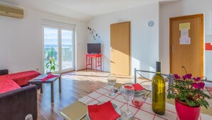 Ein Essbereich mit Tisch für zwei Personen, einem Fernseher im Hintergrund und einem Balkon mit Blumentöpfen.