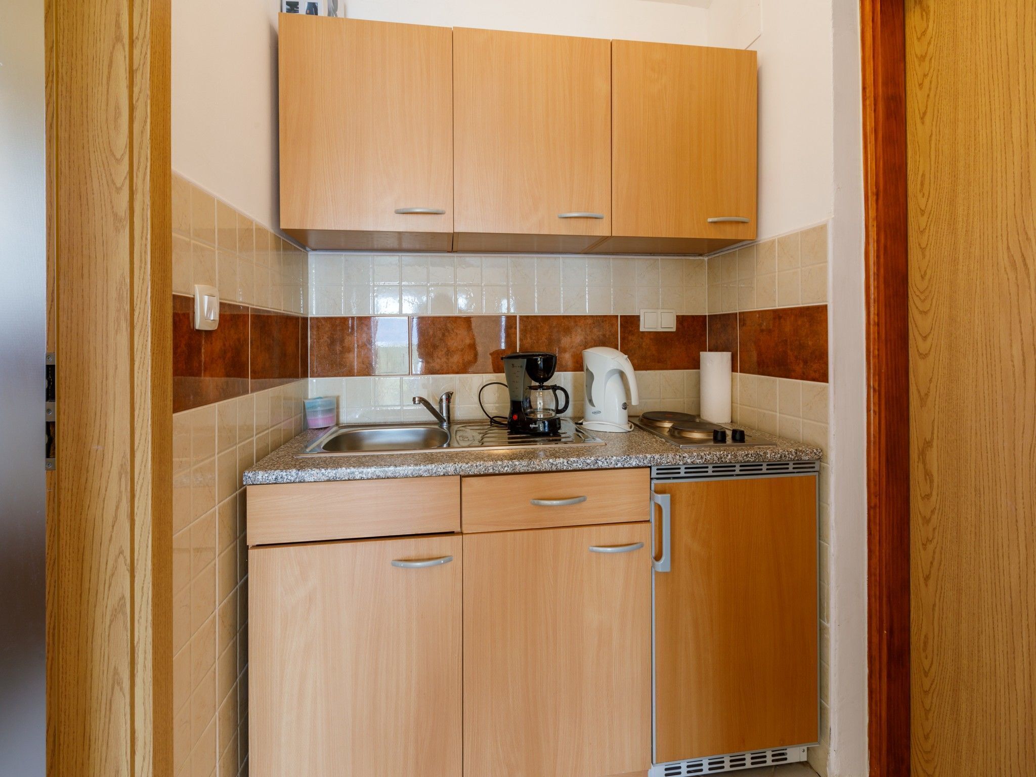 A compact kitchen with wooden cabinets, a granite countertop, a coffee maker, and a kettle.