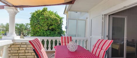 An outdoor patio with a table and chairs, a white column, a stone wall, and a large tree in the background.