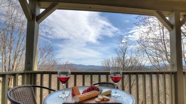 Een tafel met een kaasplank, druiven en wijnglazen op een balkon met uitzicht op de bergen.