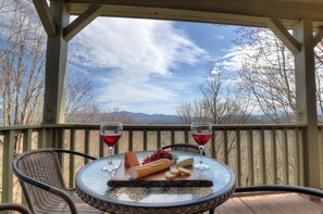 A table with a cheese board, grapes, and wine glasses on a balcony with a mountain view. - 5-STAR HOME WITH LONG RANGE VIEW, PAVED TO THE DOOR ACCOMODATES 5 LARGE VEHICLES (Franklin)
