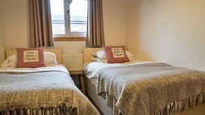 Ett rum med två sängar, var och en med en kudde och ett täcke. Det finns ett fönster med gardiner, och ett element syns på väggen.