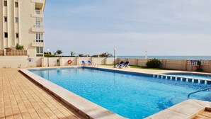 Una piscina con vista despejada al océano, rodeada por una terraza con baldosas y sillas de descanso.