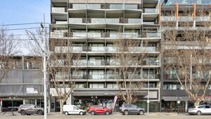 Un immeuble à plusieurs étages doté de balcons, d’une devanture de magasin et de voitures garées.