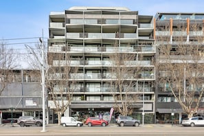 A multi-story building with balconies, a storefront, and parked cars.