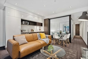 A modern living room with a leather sofa, a glass coffee table, and a dining area with a glass table and chairs.
