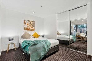 Une chambre d’hôtel moderne, équipée d’un lit, d’une table de chevet, d’une lampe et d’un grand miroir qui reflète la pièce.