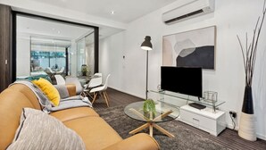 Un salon moderne avec un canapé, une table basse en verre, un téléviseur et, au fond, un coin repas.