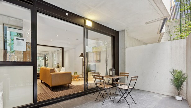 Un intérieur moderne avec une cloison en verre, un coin repas comprenant des chaises et une table, et un canapé en arrière-plan.