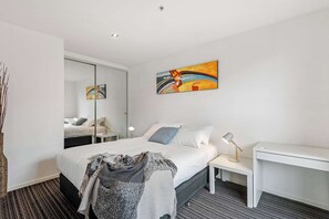 Ett modernt hotellrum med en säng, ett nattduksbord, ett skrivbord och en stor spegel.
