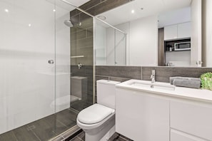 Un bagno moderno con box doccia in vetro, un water bianco e un lavandino con specchio sopra.