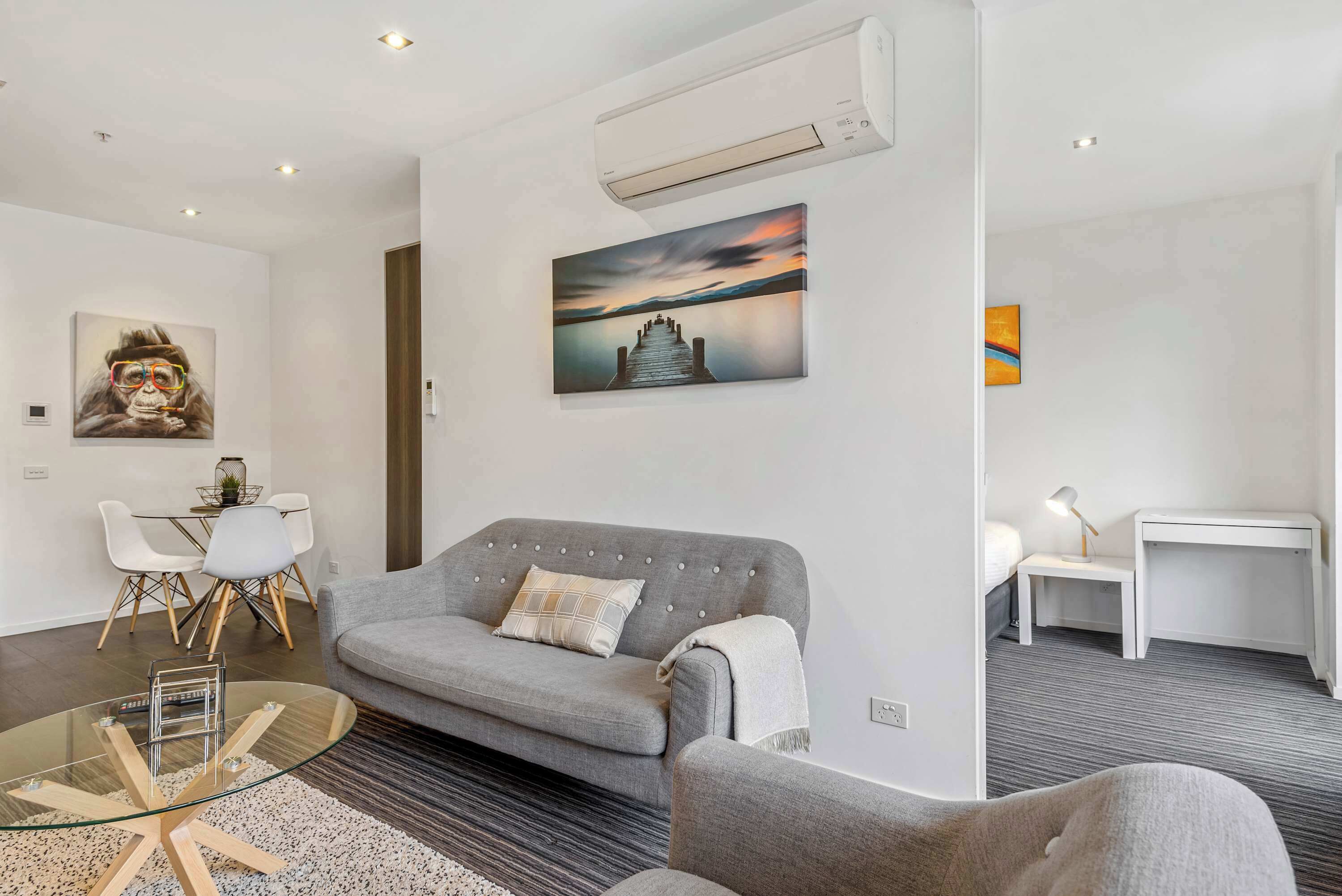 Ein modernes Wohnzimmer mit einem grauen Sofa, einem Glastisch und einem Sonnenuntergangsbild an der Wand.
