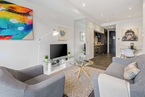 Un salon moderne avec un téléviseur à écran plat, des canapés gris, une table basse en verre et des œuvres d’art accrochées aux murs.