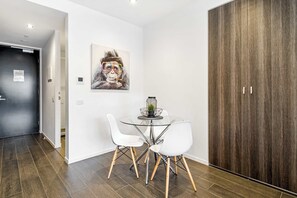Un espace repas moderne avec une table en verre, des chaises blanches, un tableau au mur et une armoire en bois.