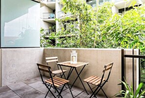 Un balcone con due sedie di legno e un tavolino, circondato da piante verdi rigogliose.