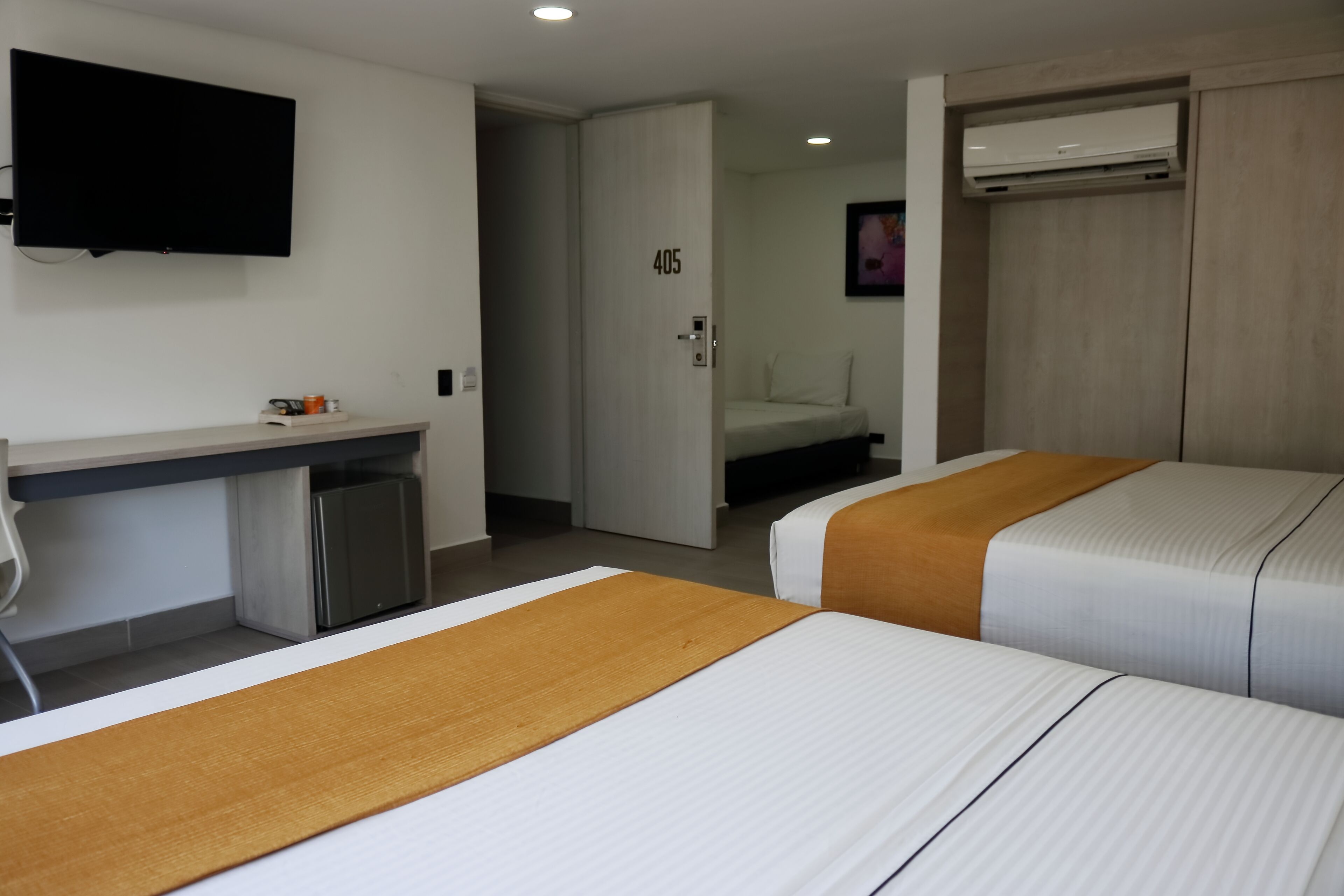 A hotel room with two beds, a desk, a television, and an air conditioning unit.