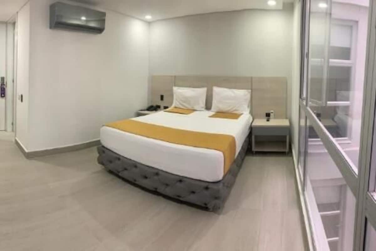 A modern hotel room with a bed, bedside table, and a desk.
