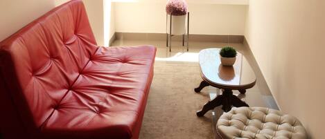 A modern living room with a red sofa, a small round table with a plant, and a white ottoman.