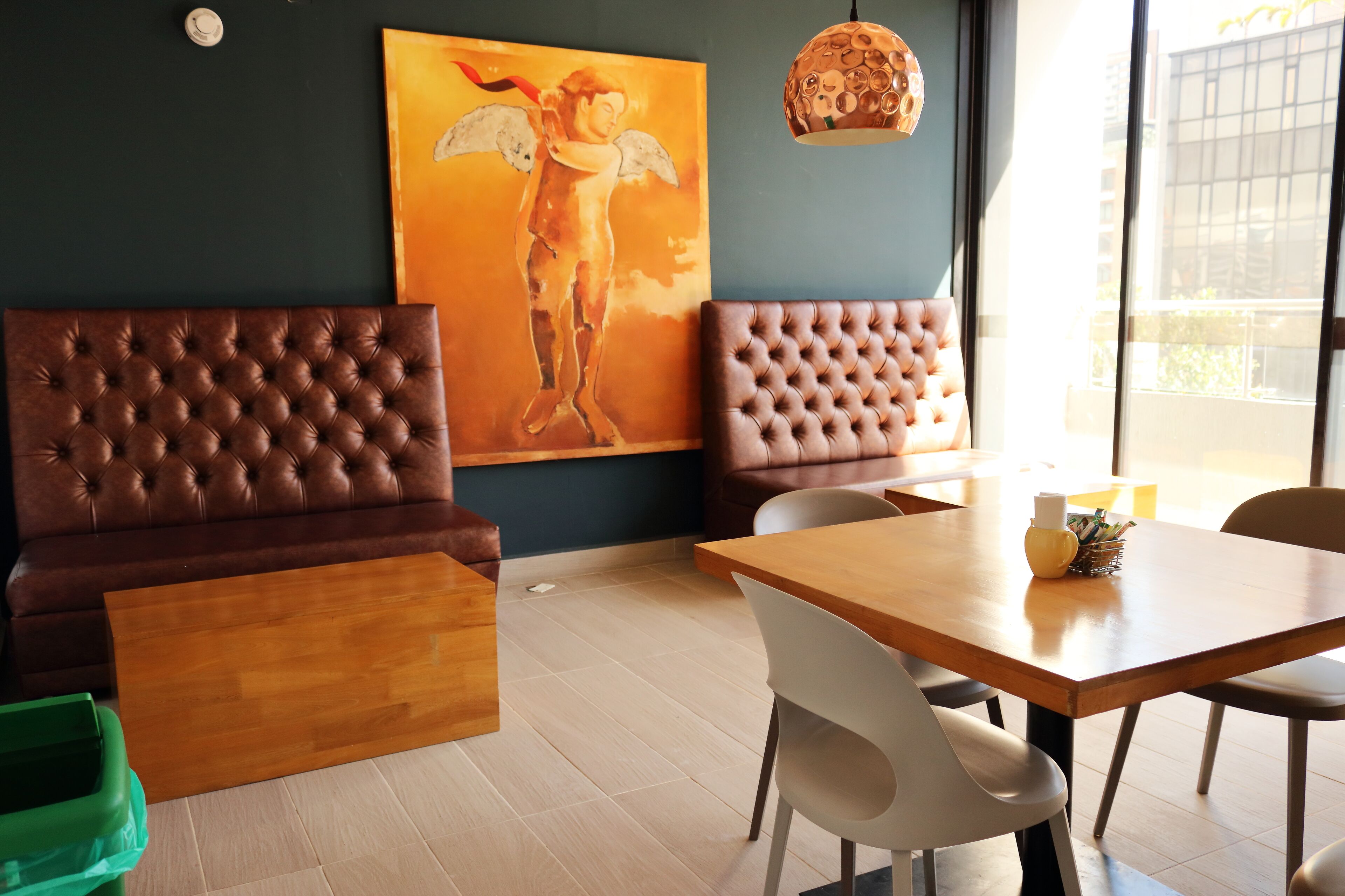 Una habitación moderna con un ventanal grande, una mesa de madera, dos sofás de cuero y un cuadro de un ángel.