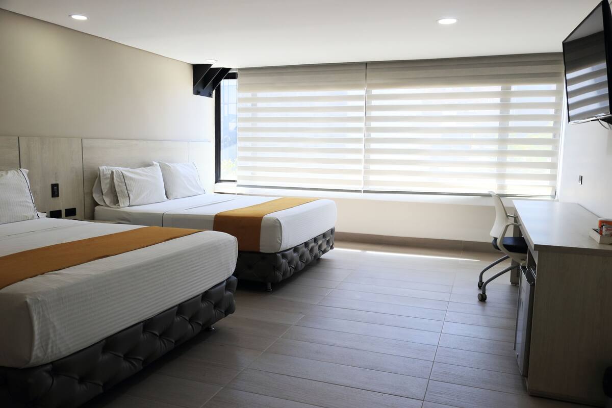 A hotel room with two beds, a desk, and a TV.