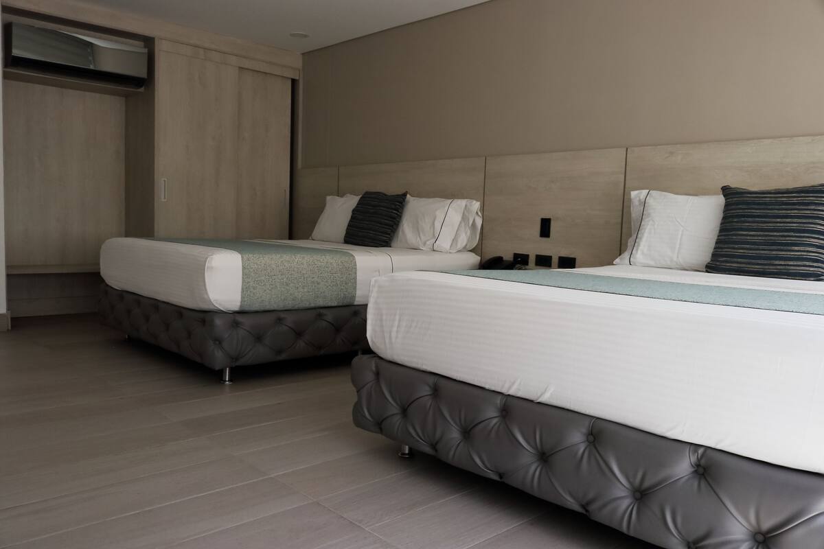 A hotel room with two beds, a wardrobe, and a built-in air conditioning unit.
